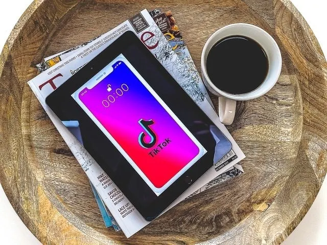 Mobiles Gerät auf einem TikTok-Bildschirm auf einer Zeitschrift neben einer Tasse Kaffee