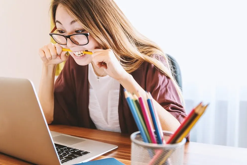 woman biting a pencil and looking at computer screen