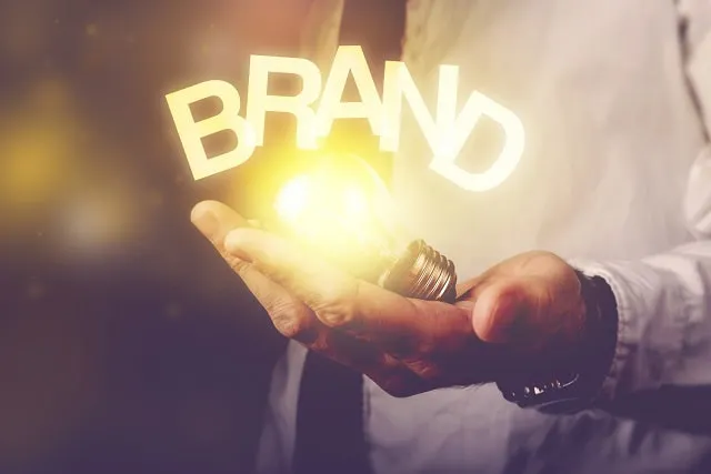 ブランド」という言葉のオーバーレイの下に電球を持つビジネスパーソン。ブランド認識のコンセプト。 