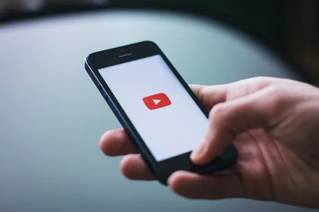 YouTubeの再生アイコンが表示された携帯電話を持つ手