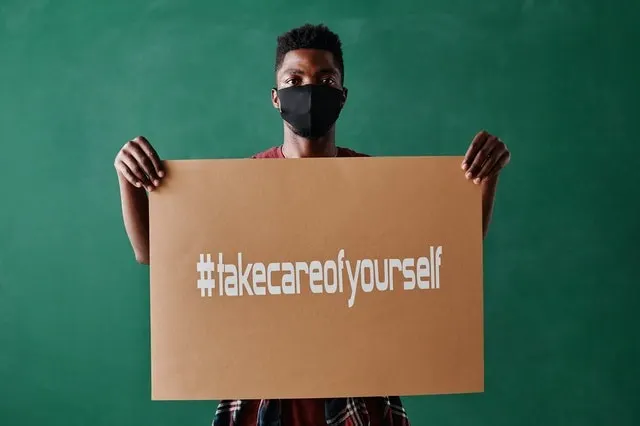 Uomo che indossa una maschera facciale con un cartello con l'hashtag #takecareofyourself 