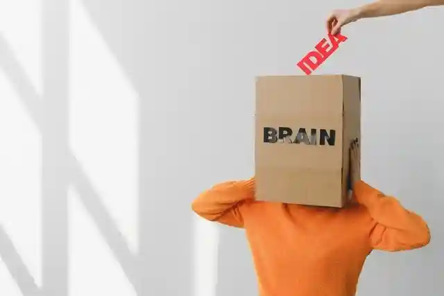 Hand placing the word "IDEA" in a box that says "BRAIN" on a person's head