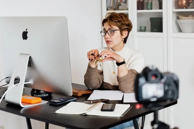 Femme enregistrant le contenu d'un cours en ligne à un bureau avec un ordinateur et une caméra.