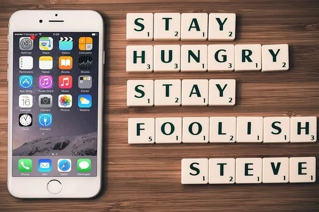 Lettere di Scarabeo che scrivono "Stay hungry. Rimanete sciocchi". Citazione di Steve Jobs accanto a un dispositivo mobile