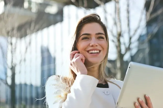 Femme souriante communiquant avec une marque au téléphone tout en tenant une tablette.